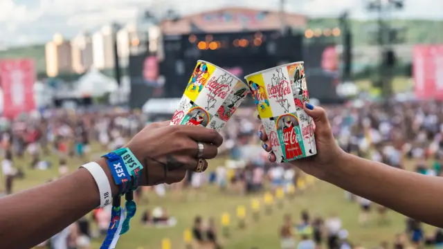 Duas pessoas brindam com os copos Coca-Cola dentro do festival
